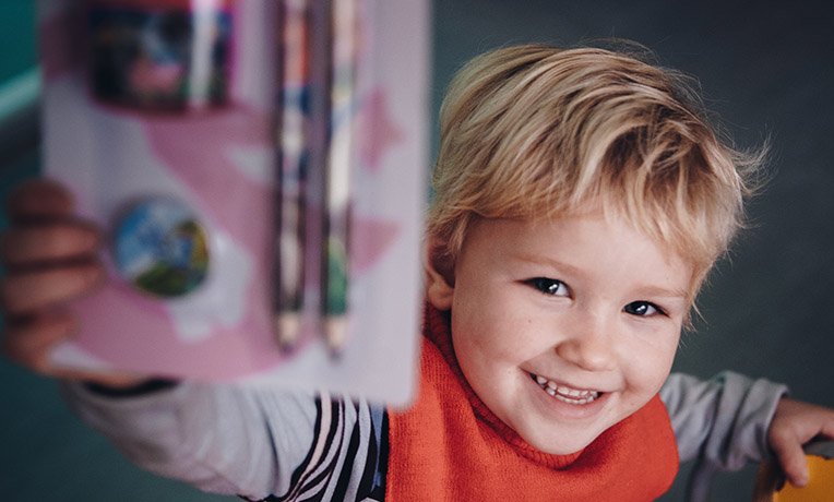 Smiling child shows stationery to camera
