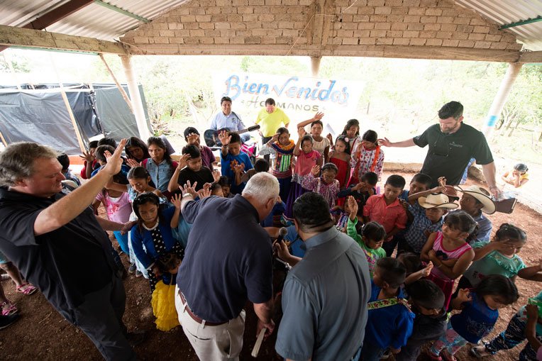 CHILDREN, CHURCH LEADERS, EDWARD GRAHAM, AND OTHERS GATHER TOGETHER AS JIM HARRELSON (CENTER IN BLUE SHIRT) LEADS IN PRAYER DURING THE CHURCH DEDICATION.