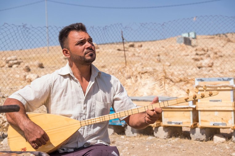 A Yazidi serenades the bees he received from Samaritan’s Purse.