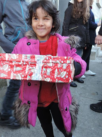 Girl in pink coat smiles with wrapped shoebox gift