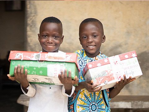 two children holding shoebox gifts