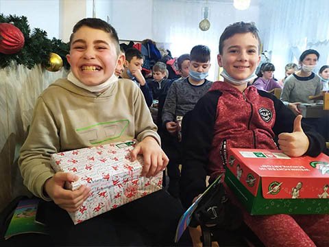 two boys smile with shoebox gifts, one gives thumbs up